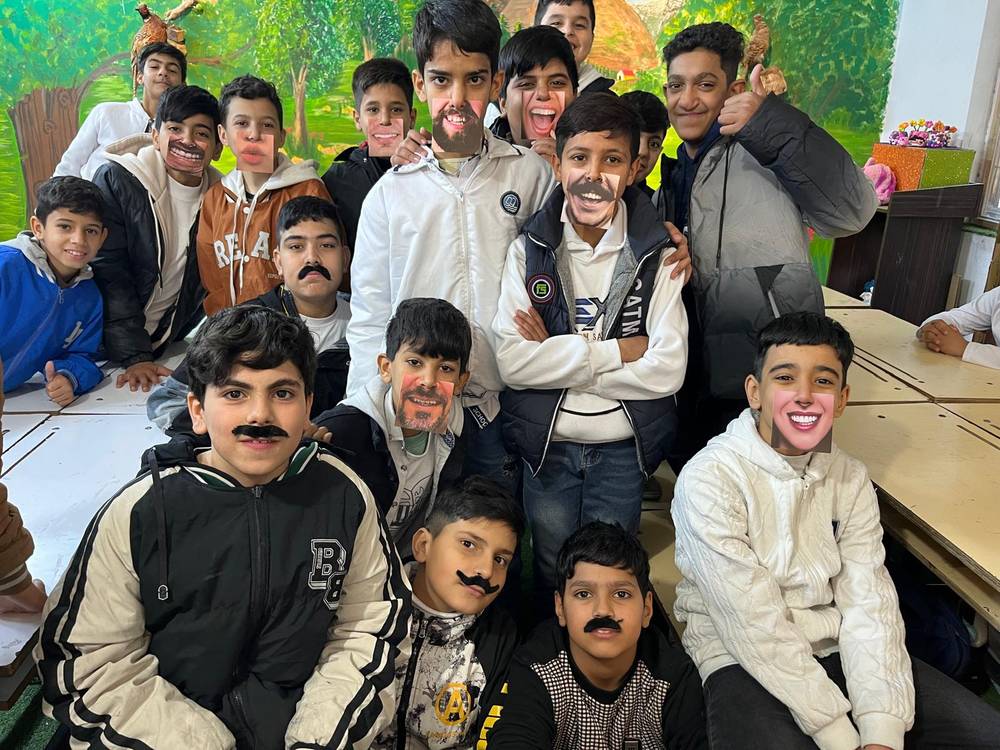 Boys laughing with paper moustaches in an art workshop