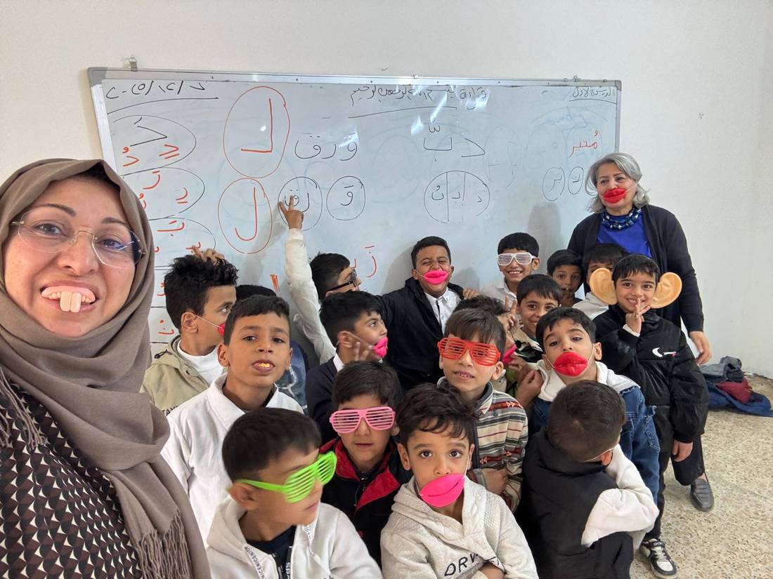A volunteer and laughing boys in funny glasses during a classroom workshop